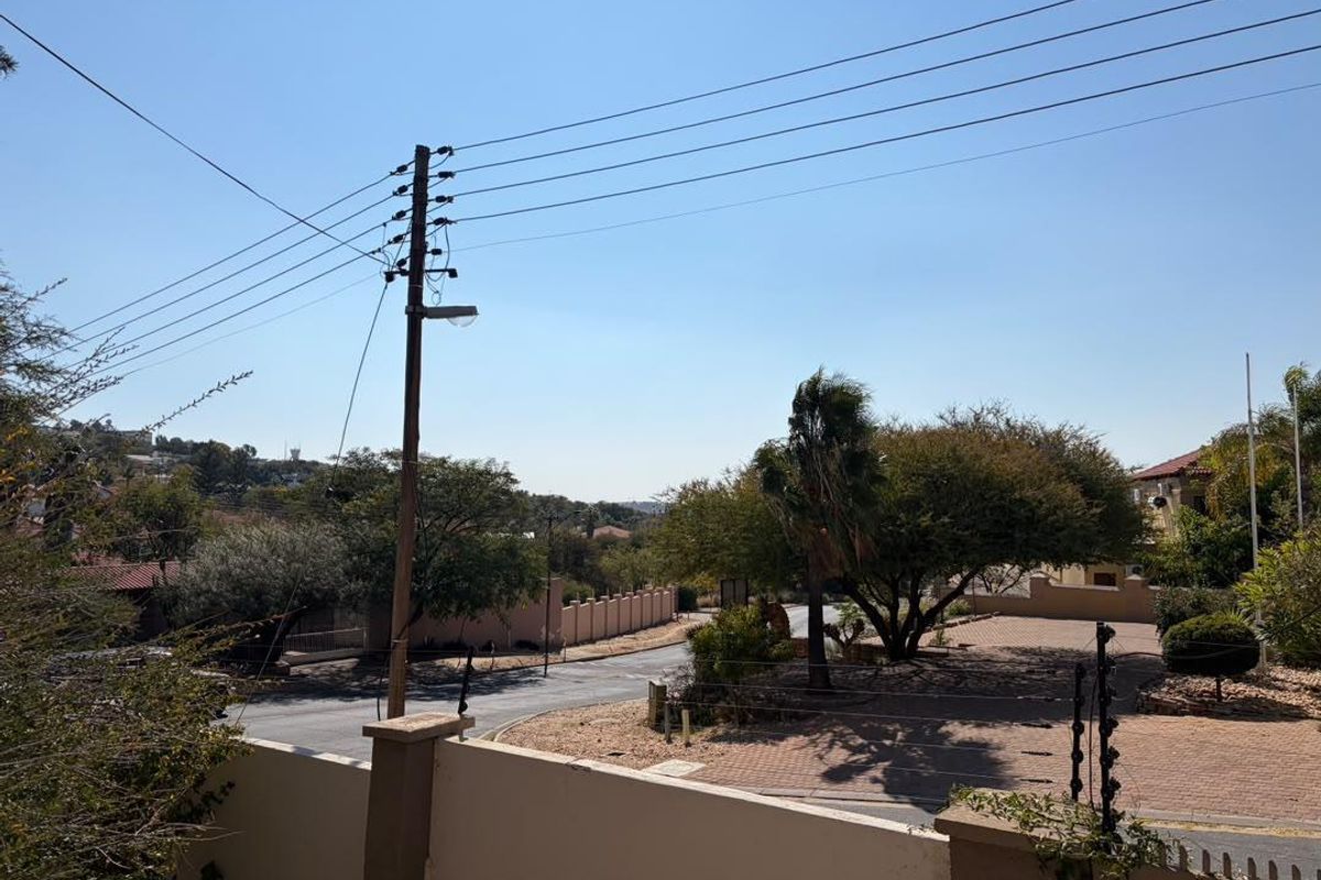 An elevated street view showing the property entrance, paved driveway, perimeter wall with electric fencing, and surrounding neighbourhood landscape.