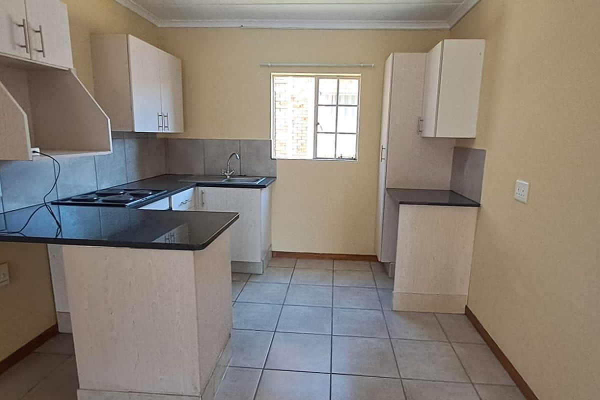 A functional kitchen featuring laminate cabinetry, granite countertops, an electric hob, and tiled flooring, offering a clean and practical workspace.