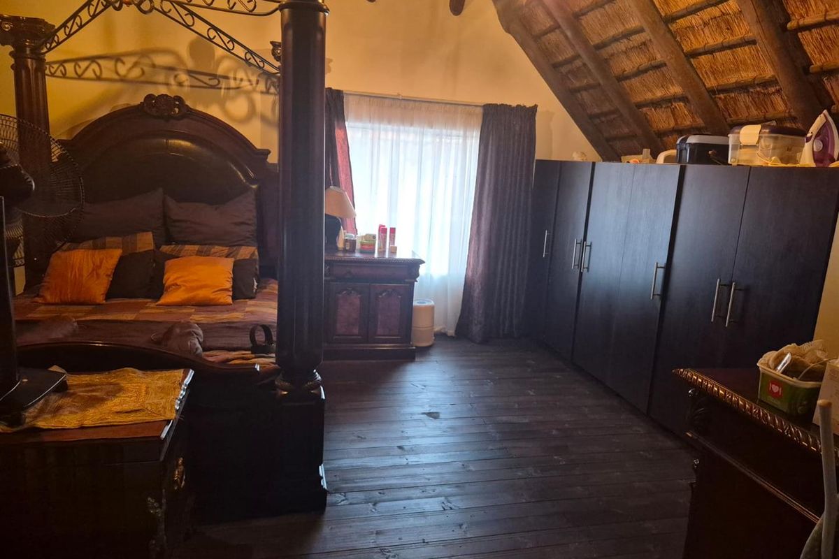 Spacious bedroom featuring exposed thatched roof rafters, dark timber flooring, and built-in cabinetry, creating a rustic and cozy atmosphere.