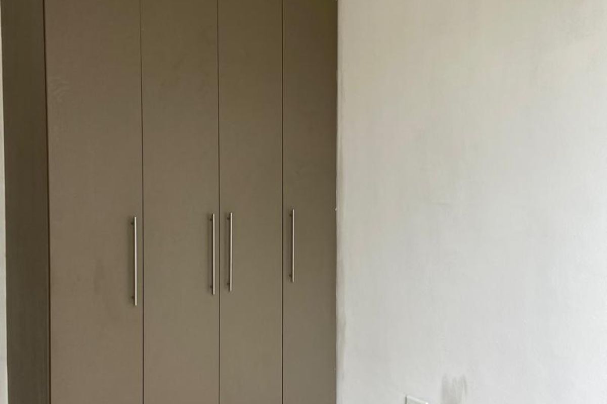 A clean, empty bedroom featuring a modern built-in wardrobe with matte brown finish and neutral tiled flooring.