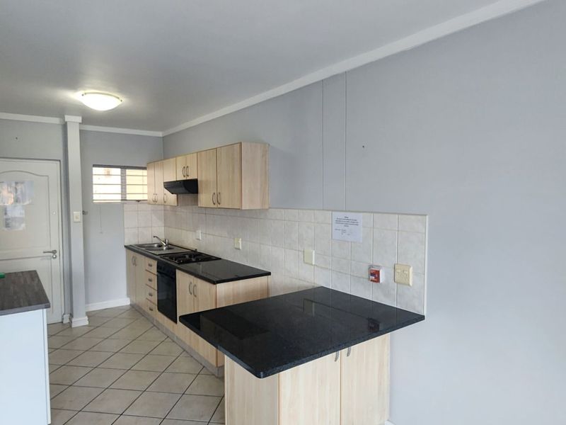 A functional kitchen featuring light wood cabinetry, dark countertops, a built-in oven and hob, and tiled flooring in an open-plan layout.