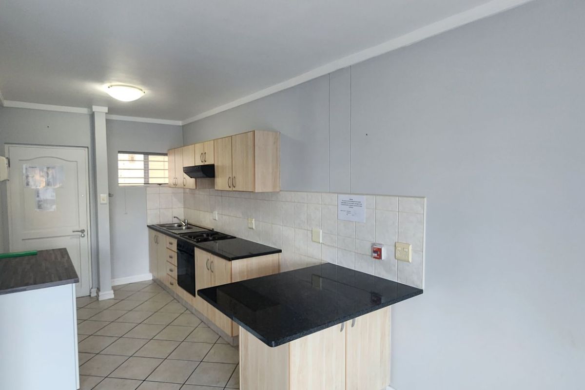 A functional kitchen featuring light wood cabinetry, dark countertops, a built-in oven and hob, and tiled flooring in an open-plan layout.