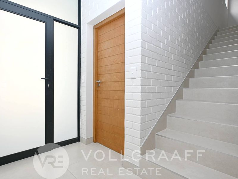 A bright and modern entrance area featuring a clean staircase, tiled flooring, and a contemporary glass door with a painted brick accent wall.