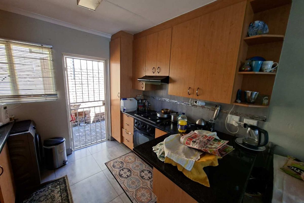 Functional kitchen featuring wooden cabinetry, built-in oven and hob, tiled flooring, and direct access to an outdoor area through a security gate.
