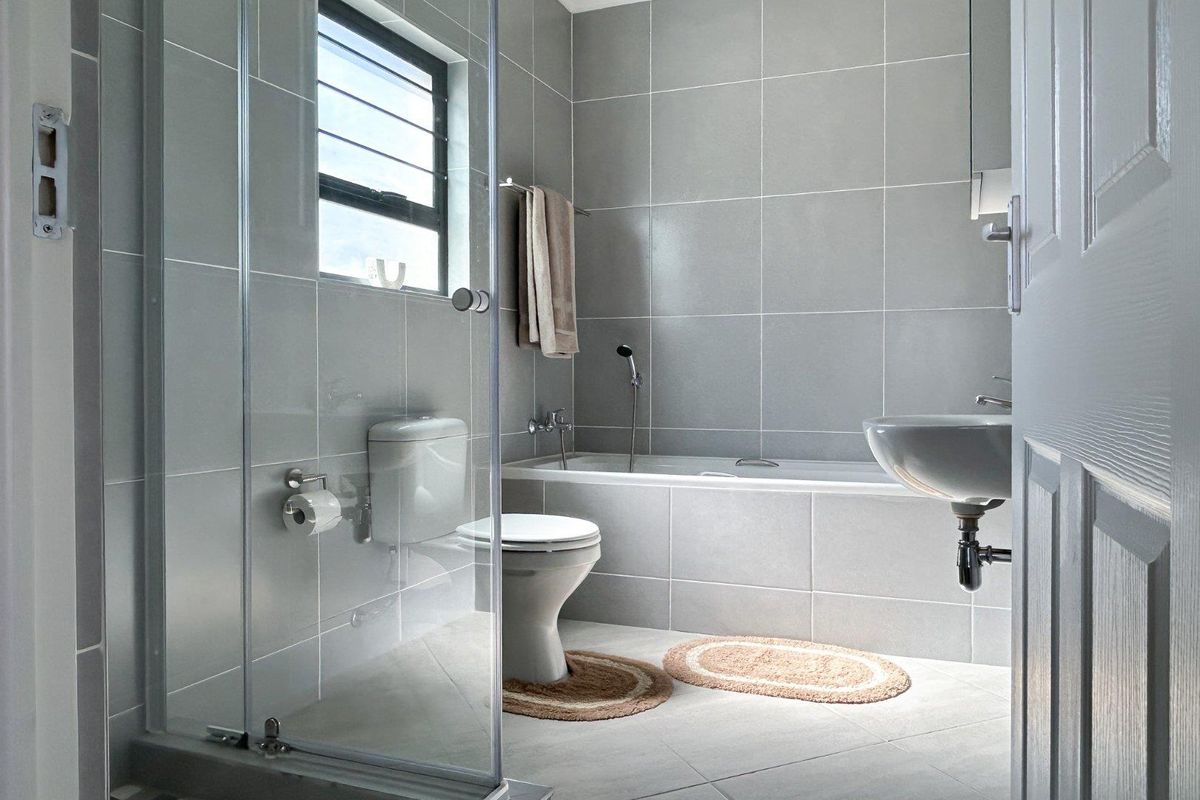 Modern bathroom featuring floor-to-ceiling grey tiling, a glass-enclosed shower, a built-in bathtub, and a wall-mounted basin.