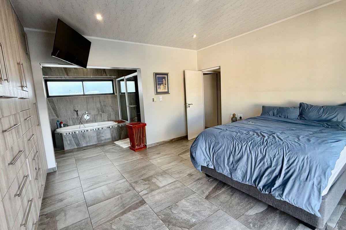 Spacious open-plan bedroom featuring integrated cabinetry, tiled flooring, and an en-suite bathroom area with a built-in bathtub and shower.
