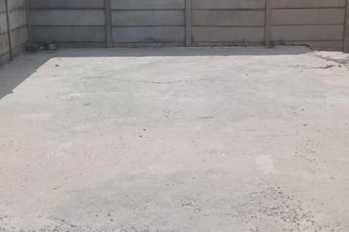 A paved outdoor area enclosed by precast concrete boundary walls, featuring a concrete slab surface.