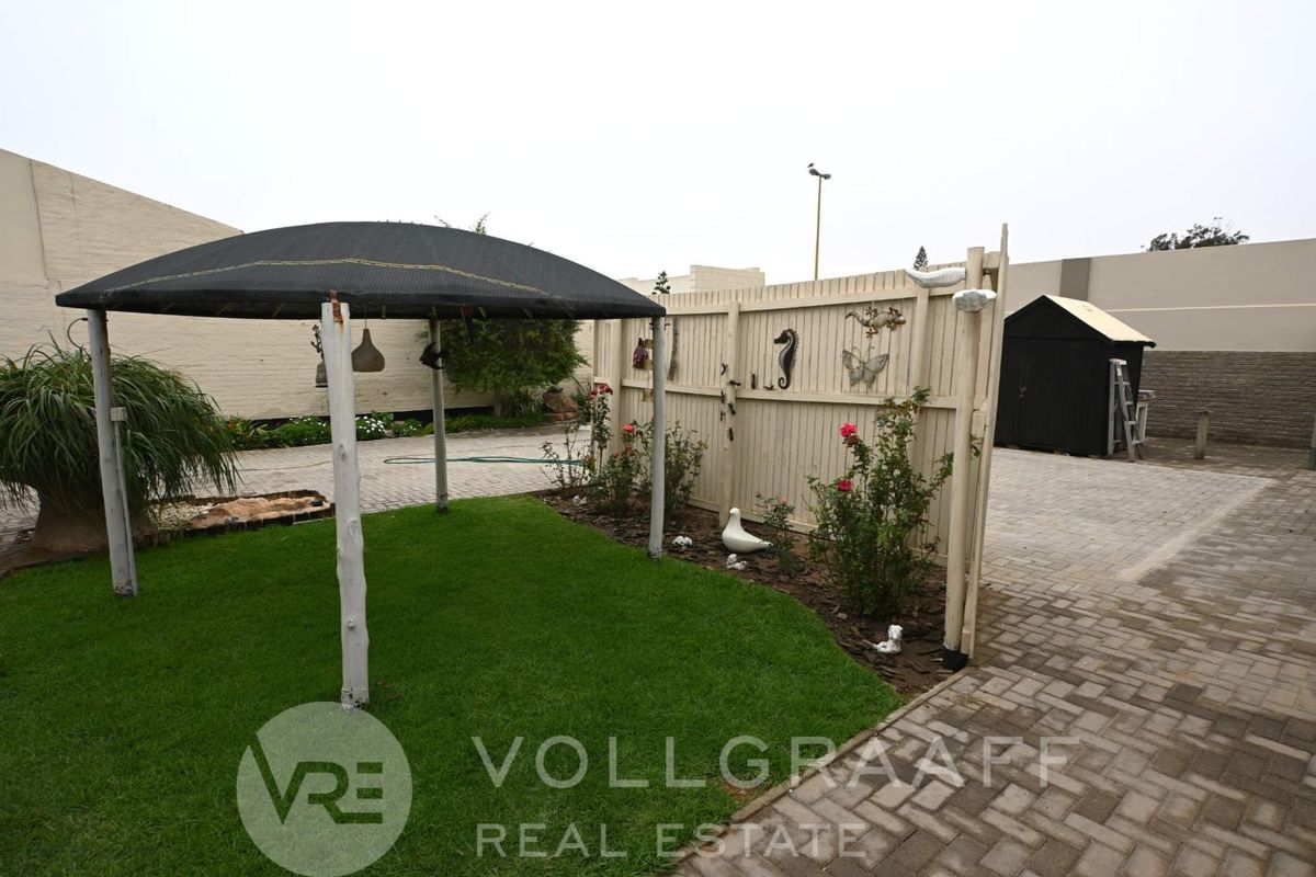A private rear garden area featuring a paved driveway, a small lawn, a gazebo, and a timber privacy screen.