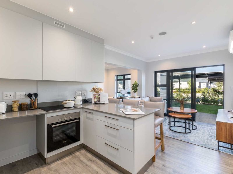 Modern open-plan kitchen and living area featuring sleek cabinetry, stone countertops, integrated appliances, and seamless access to a private patio through sliding glass doors.