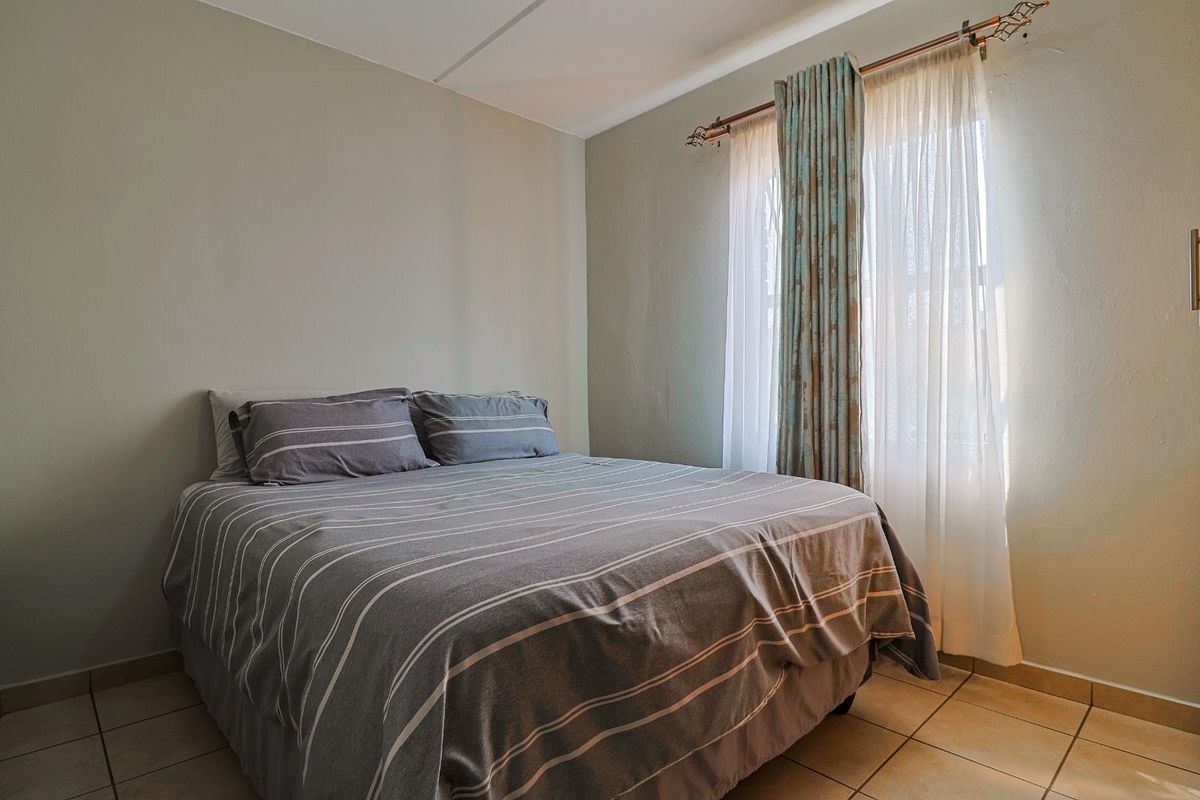 A functional bedroom featuring tiled flooring and a window with a fitted curtain rod, providing a neutral space ready for personalization.