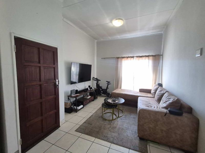 A functional living room featuring tiled flooring, a timber entrance door, and a large window with a curtain rail.