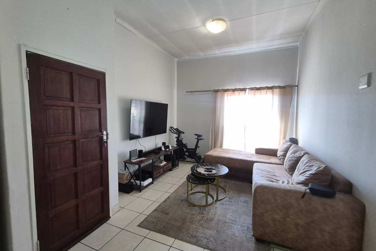 A functional living room featuring tiled flooring, a timber entrance door, and a large window with a curtain rail.