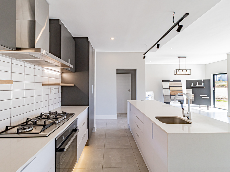 Modern kitchen featuring a central island with sink, gas hob, built-in oven, extractor fan, and sleek cabinetry with subway tile backsplash.