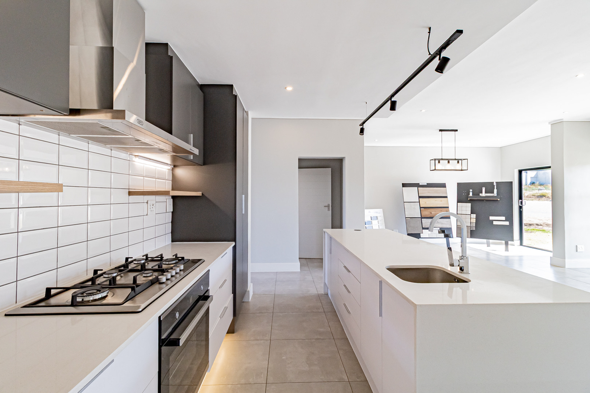Modern kitchen featuring a central island with sink, gas hob, built-in oven, extractor fan, and sleek cabinetry with subway tile backsplash.