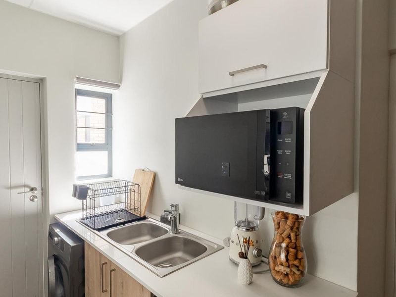 A functional scullery area featuring a double basin stainless steel sink, laminate countertops, and built-in cabinetry with integrated microwave housing.