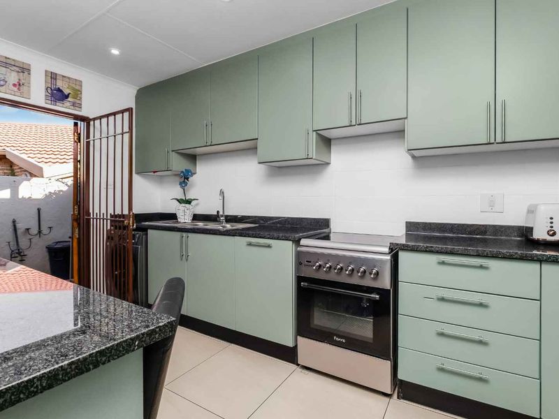 A well-maintained kitchen featuring sage green cabinetry, granite countertops, stainless steel oven, and tiled flooring with direct access to an outdoor area.