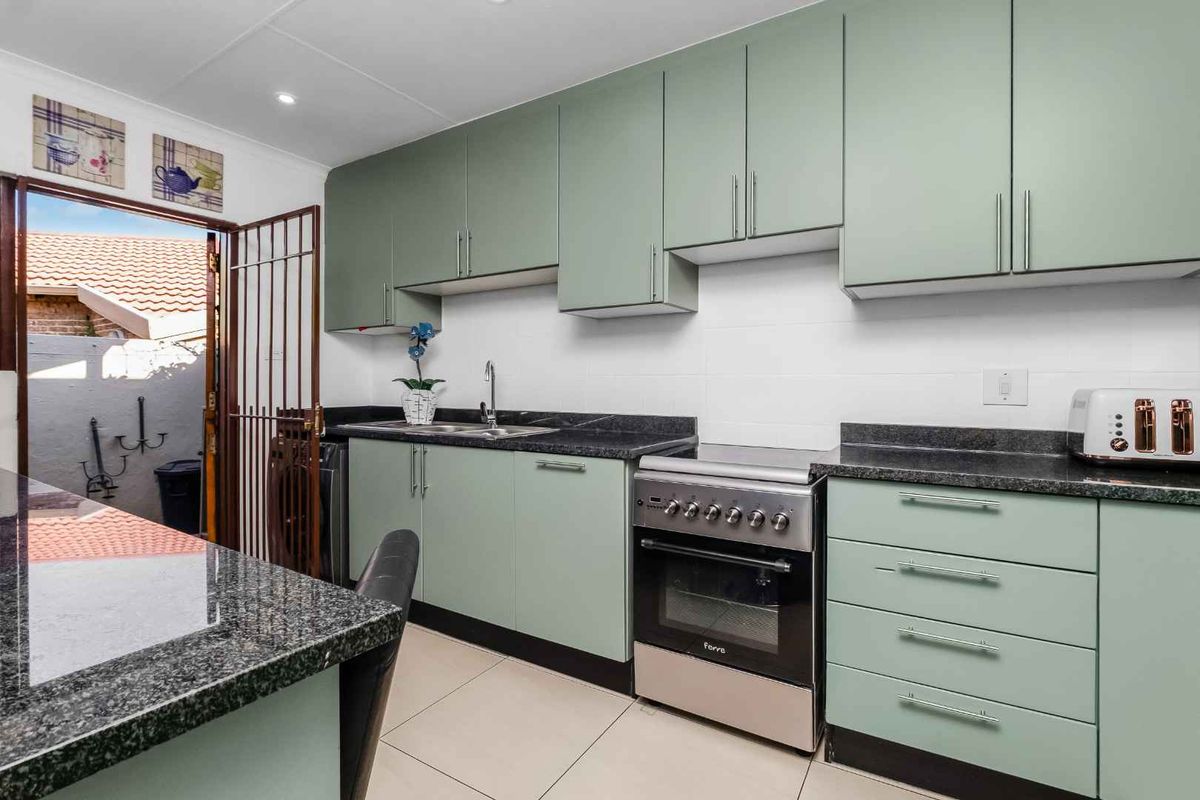A well-maintained kitchen featuring sage green cabinetry, granite countertops, stainless steel oven, and tiled flooring with direct access to an outdoor area.