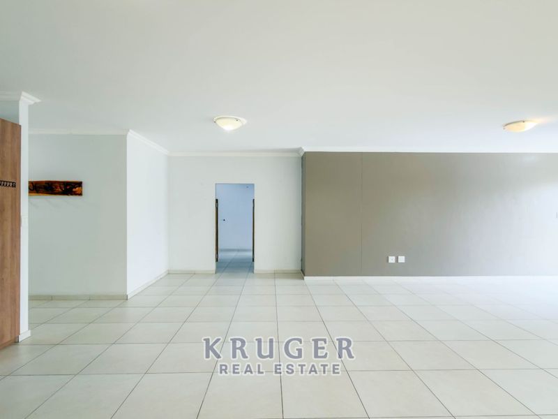 A spacious, empty living area featuring neutral tiled flooring, coved cornicing, and a built-in cupboard, offering a versatile blank canvas for interior design.