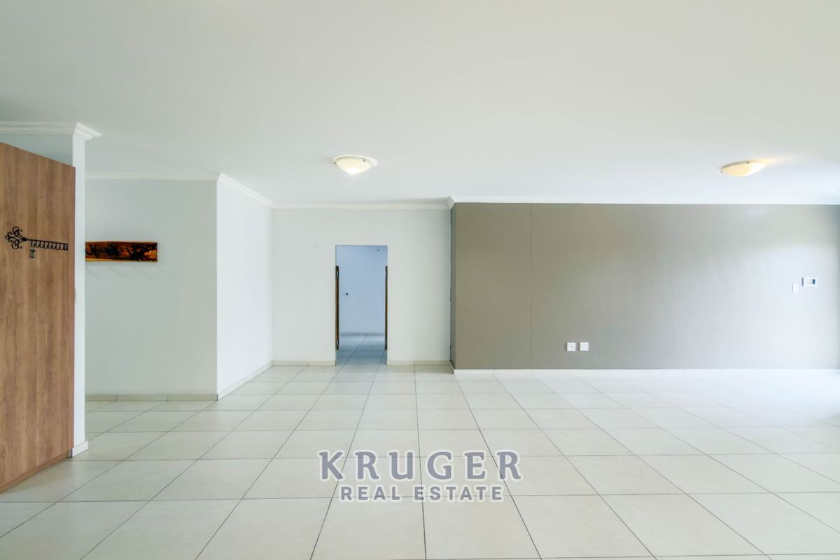 A spacious, empty living area featuring neutral tiled flooring, coved cornicing, and a built-in cupboard, offering a versatile blank canvas for interior design.