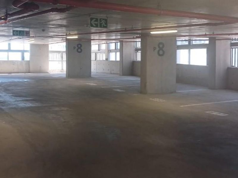 A spacious, open-plan underground parking garage featuring concrete flooring, structural columns, and exposed overhead fire safety infrastructure.