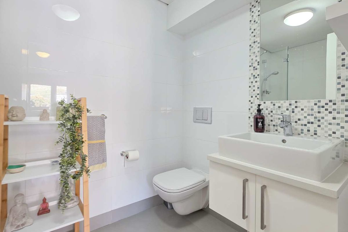Modern bathroom featuring a wall-mounted toilet, vanity with vessel sink, mosaic tile accents, and a glass-enclosed shower.