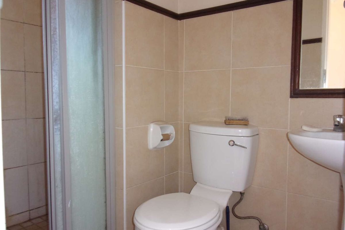 A functional bathroom featuring a shower enclosure, pedestal basin, and toilet with neutral wall tiling.