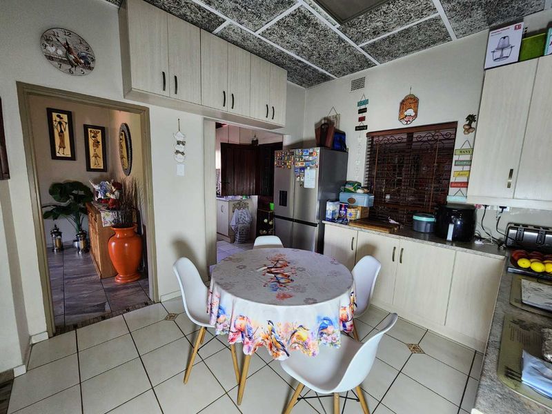 A functional kitchen featuring built-in cabinetry, laminate countertops, and tiled flooring, with an adjacent dining area and access to a secondary living space.