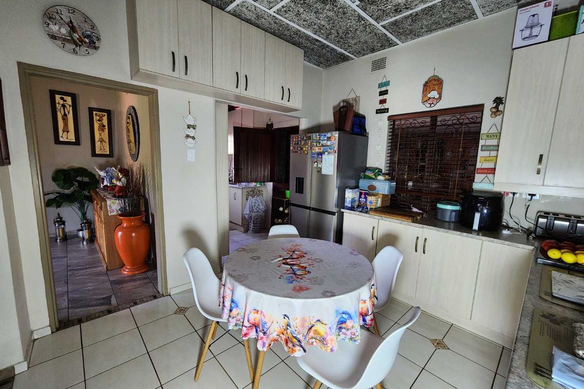 A functional kitchen featuring built-in cabinetry, laminate countertops, and tiled flooring, with an adjacent dining area and access to a secondary living space.