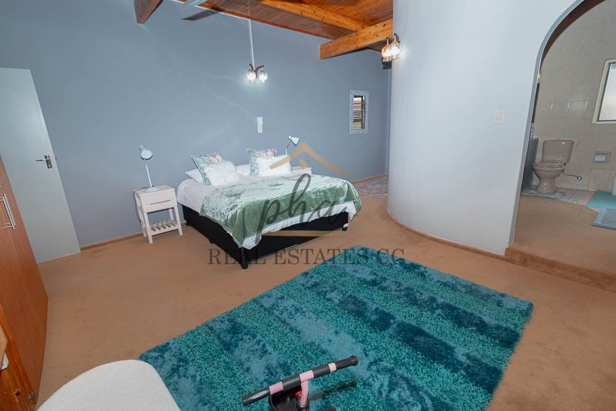 Spacious bedroom featuring exposed timber ceiling beams, an arched entryway leading to an en-suite bathroom, and neutral wall finishes.