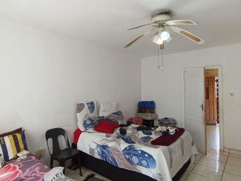 A bedroom featuring tiled flooring and a ceiling fan, providing a functional space with direct access to an adjoining hallway.