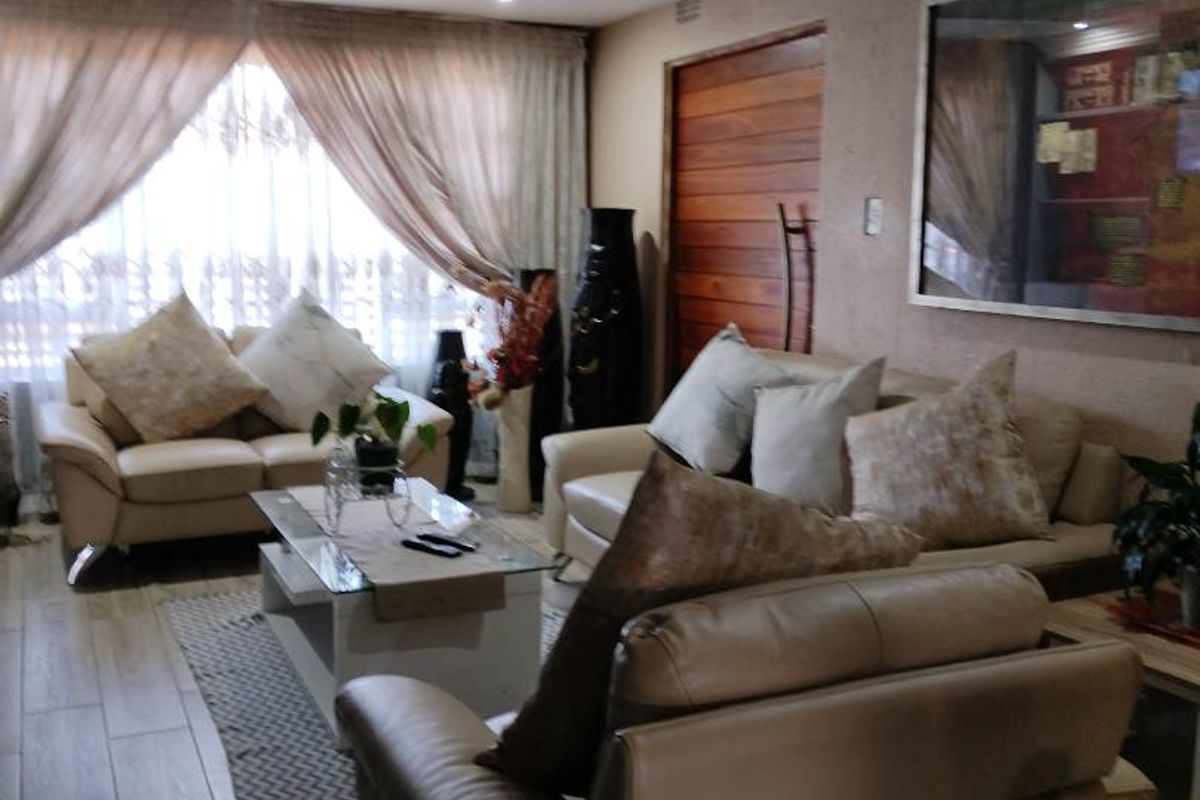 A comfortable living room featuring wood-look tiled flooring, recessed ceiling lighting, and a solid timber door, creating a warm and inviting atmosphere.