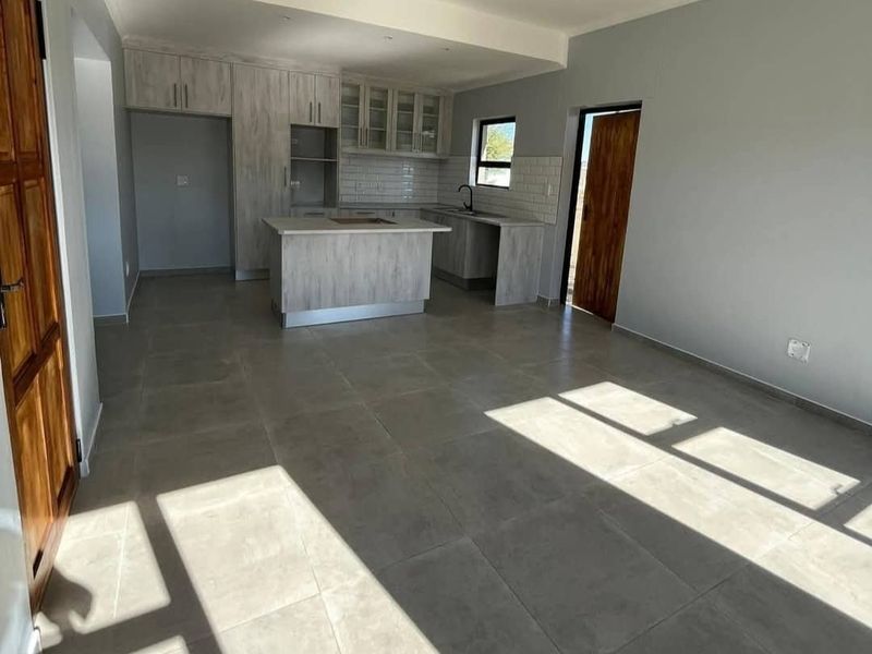 An open-plan living and kitchen area featuring modern light-wood cabinetry, a central kitchen island, subway tile backsplash, and neutral floor tiles.