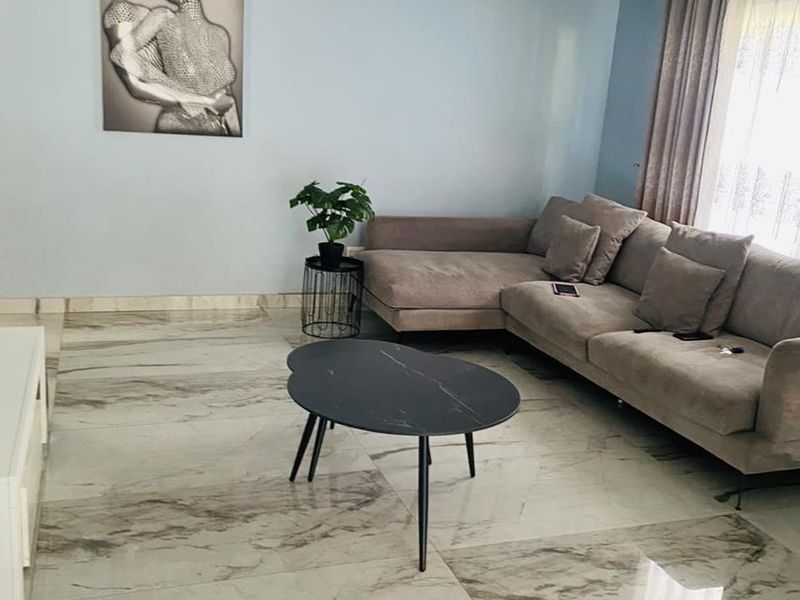 A bright living room featuring polished marble-look porcelain floor tiles, coved ceiling cornicing, and neutral wall finishes.