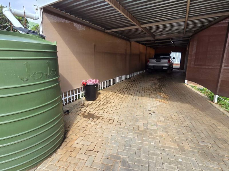 A covered carport area featuring paved flooring and a large water storage tank.