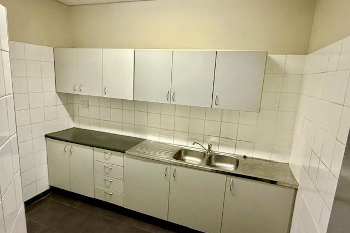 A functional office kitchenette featuring white cabinetry, a stainless steel double sink, and tiled splashbacks.