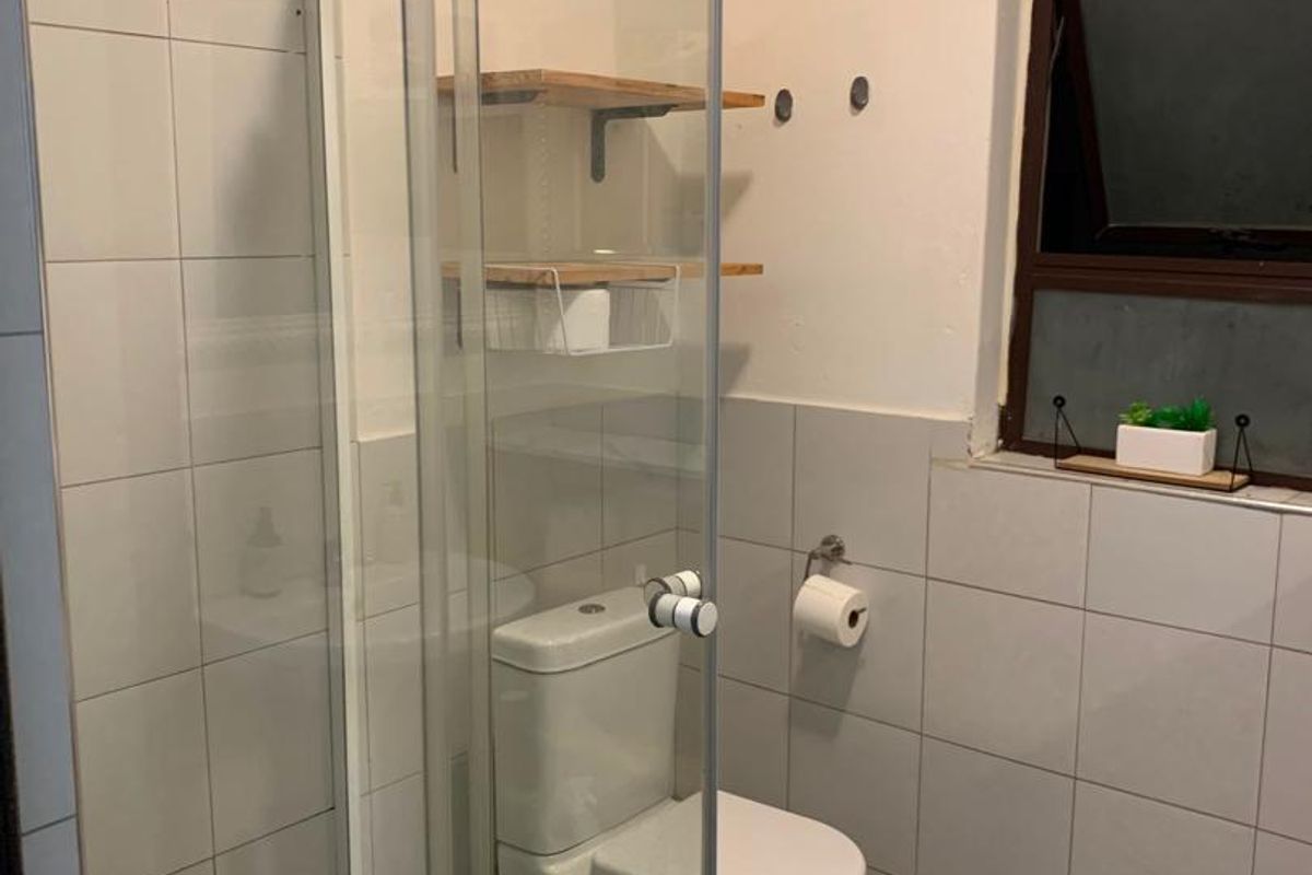 A functional bathroom featuring a glass-enclosed shower, a standard toilet, and tiled walls with a small window for ventilation.