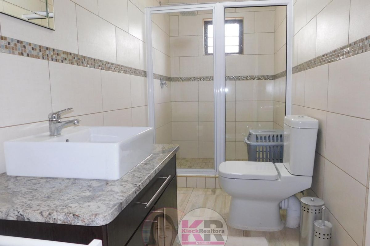 A modern bathroom featuring a granite-topped vanity with a vessel sink, a glass-enclosed shower, and neutral wall tiling.