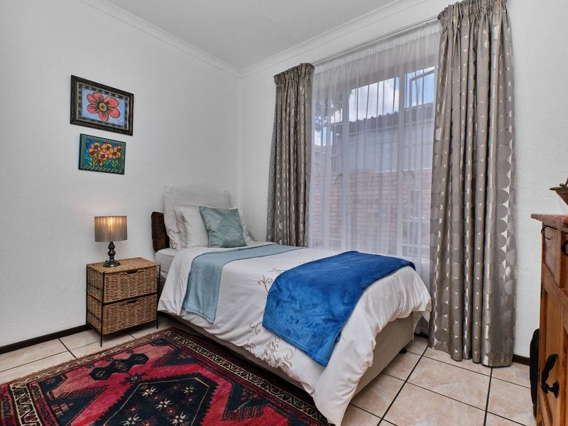 A compact bedroom featuring tiled flooring, neutral walls, and a window with curtain treatments, providing a functional and well-lit living space.