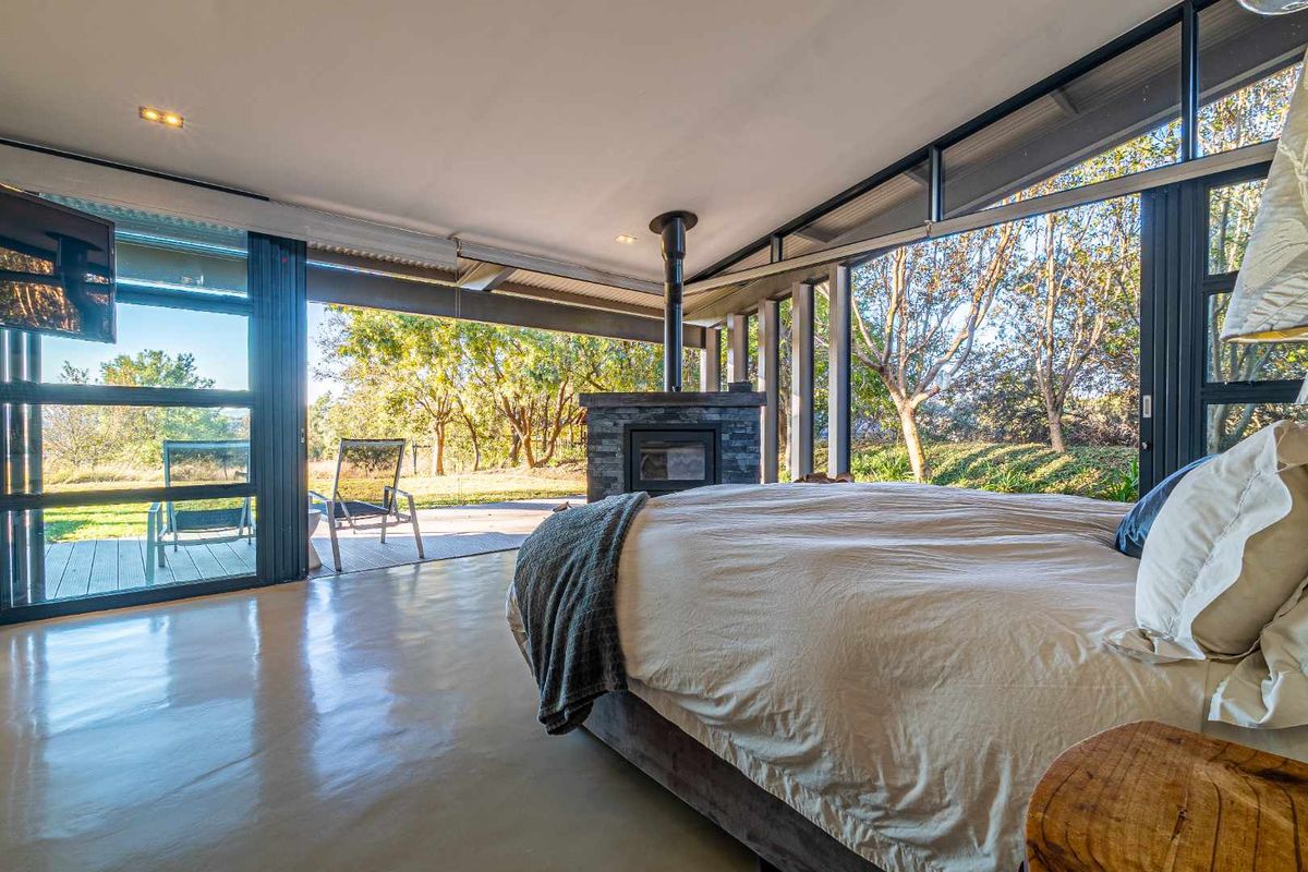 Spacious bedroom featuring polished concrete floors, a central stone-clad fireplace, and expansive floor-to-ceiling glass sliding doors opening onto a private outdoor deck.