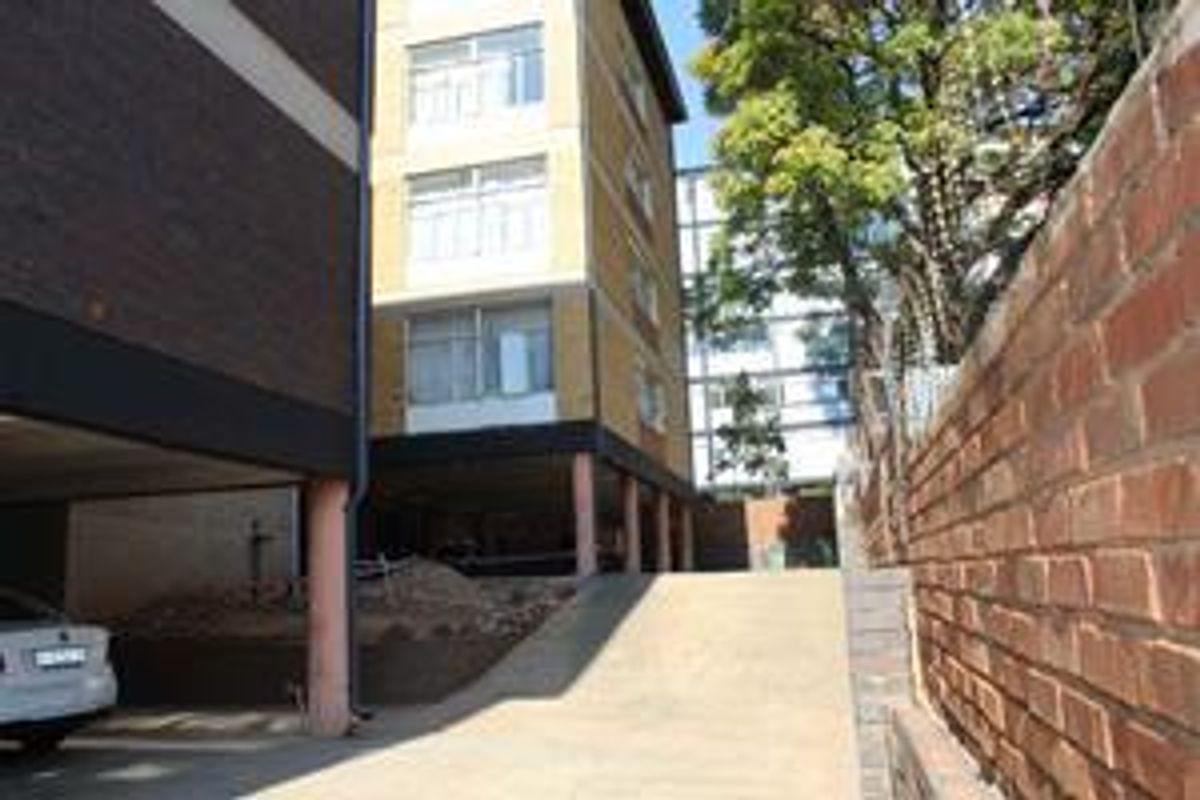 Exterior view of an apartment building featuring a concrete driveway, covered parking area, and a brick boundary wall.