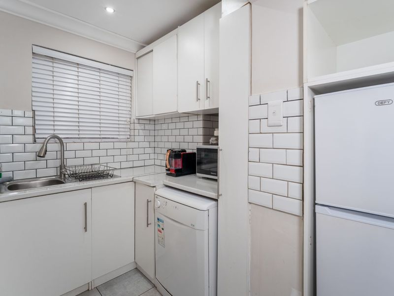 Compact kitchen featuring white cabinetry, subway tile backsplash, stainless steel sink with gooseneck faucet, and integrated appliance space.