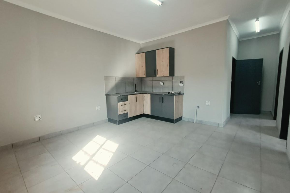 A compact, modern kitchen area featuring two-tone cabinetry, tiled flooring, and a tiled backsplash, presented in a clean, empty space.