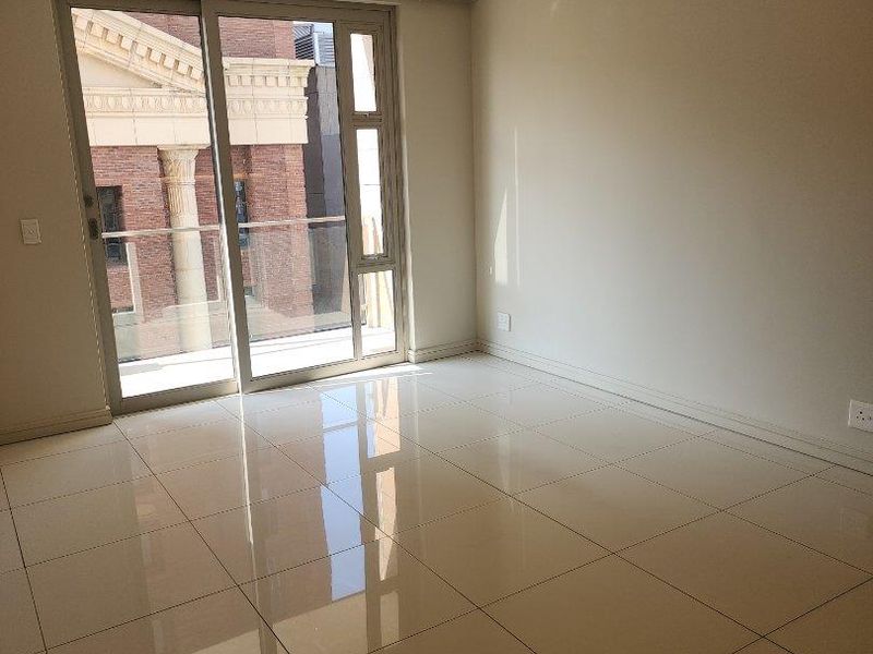 An empty, well-lit living area featuring polished tiled flooring and a large sliding glass door providing access to a balcony.