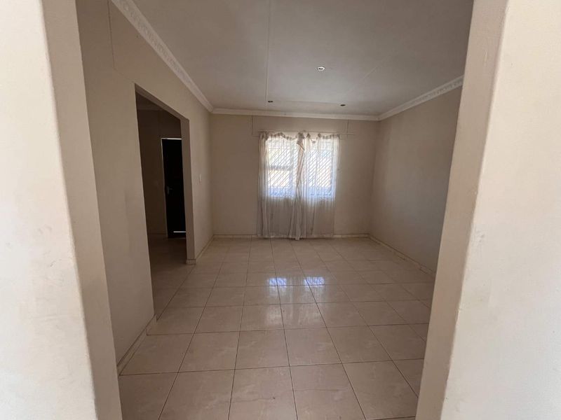 A vacant living room featuring neutral tiled flooring, decorative cornice, and security bars on the window, offering a blank canvas for interior design.