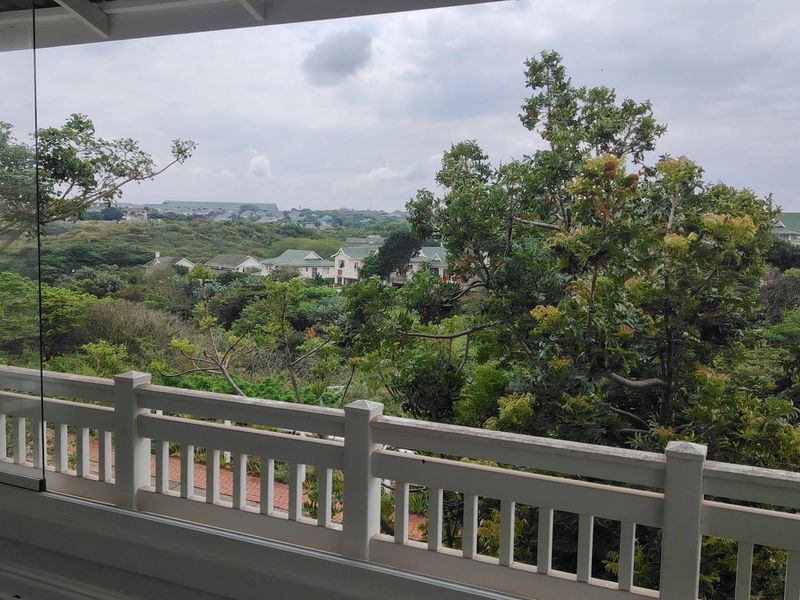 A scenic elevated view overlooking a lush green landscape and residential neighborhood, captured from a balcony with a white railing.
