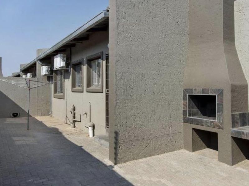 A paved outdoor patio area featuring a built-in braai, external air conditioning units, and a rotary clothesline.