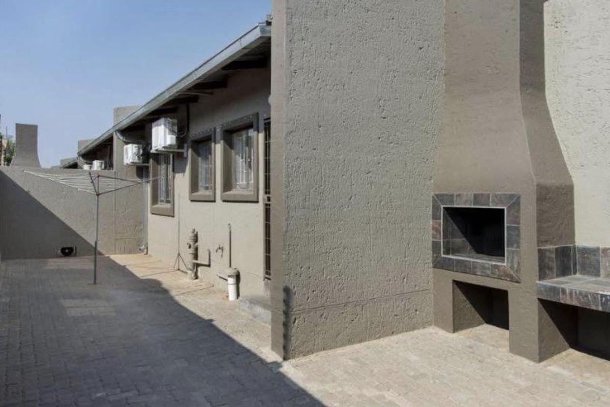 A paved outdoor patio area featuring a built-in braai, external air conditioning units, and a rotary clothesline.