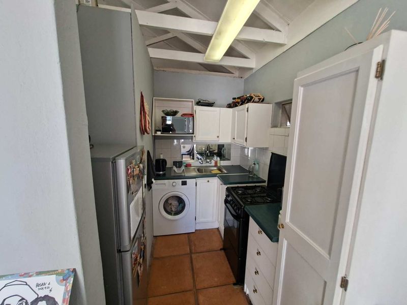 Compact kitchen featuring white cabinetry, laminate countertops, gas stove, and integrated laundry facilities under exposed timber rafters.