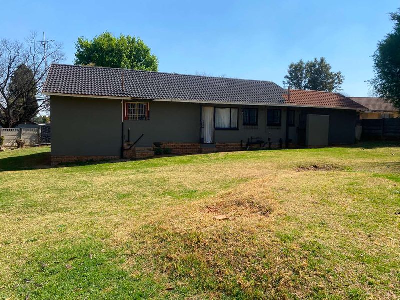 Rear view of the house featuring a tiled roof, brick foundation, and security bars on the windows, set against a large backyard.