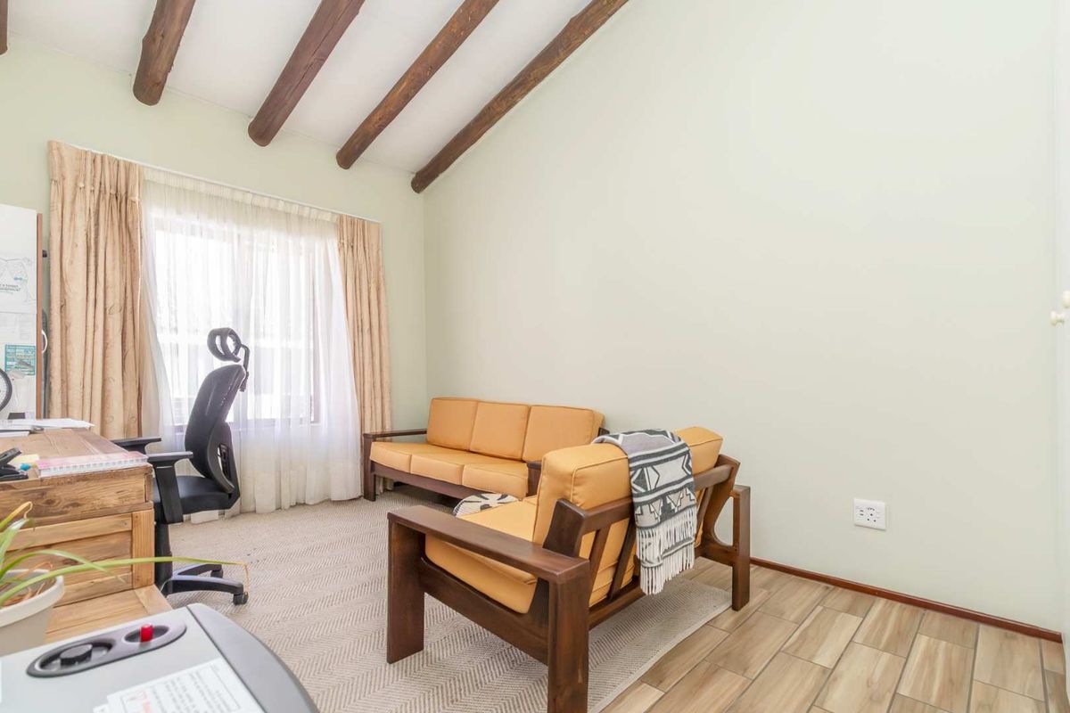 A bright living area featuring exposed timber ceiling beams, neutral walls, and tiled flooring, offering a comfortable and character-filled space.